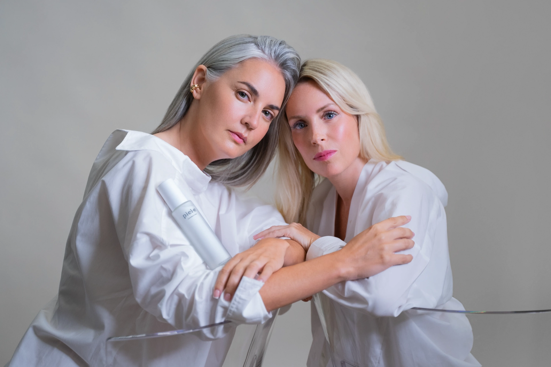 Dos mujeres vestidas con una camisa blanca posando juntas con la loción facial Esencia Calmante de Piel·e Cosmetics